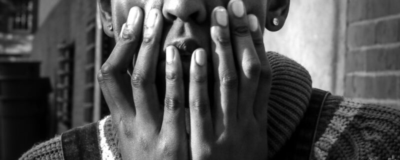 grayscale photo of man in sweater covering his face