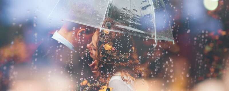 a bride and groom kiss in the rain under an umbrella